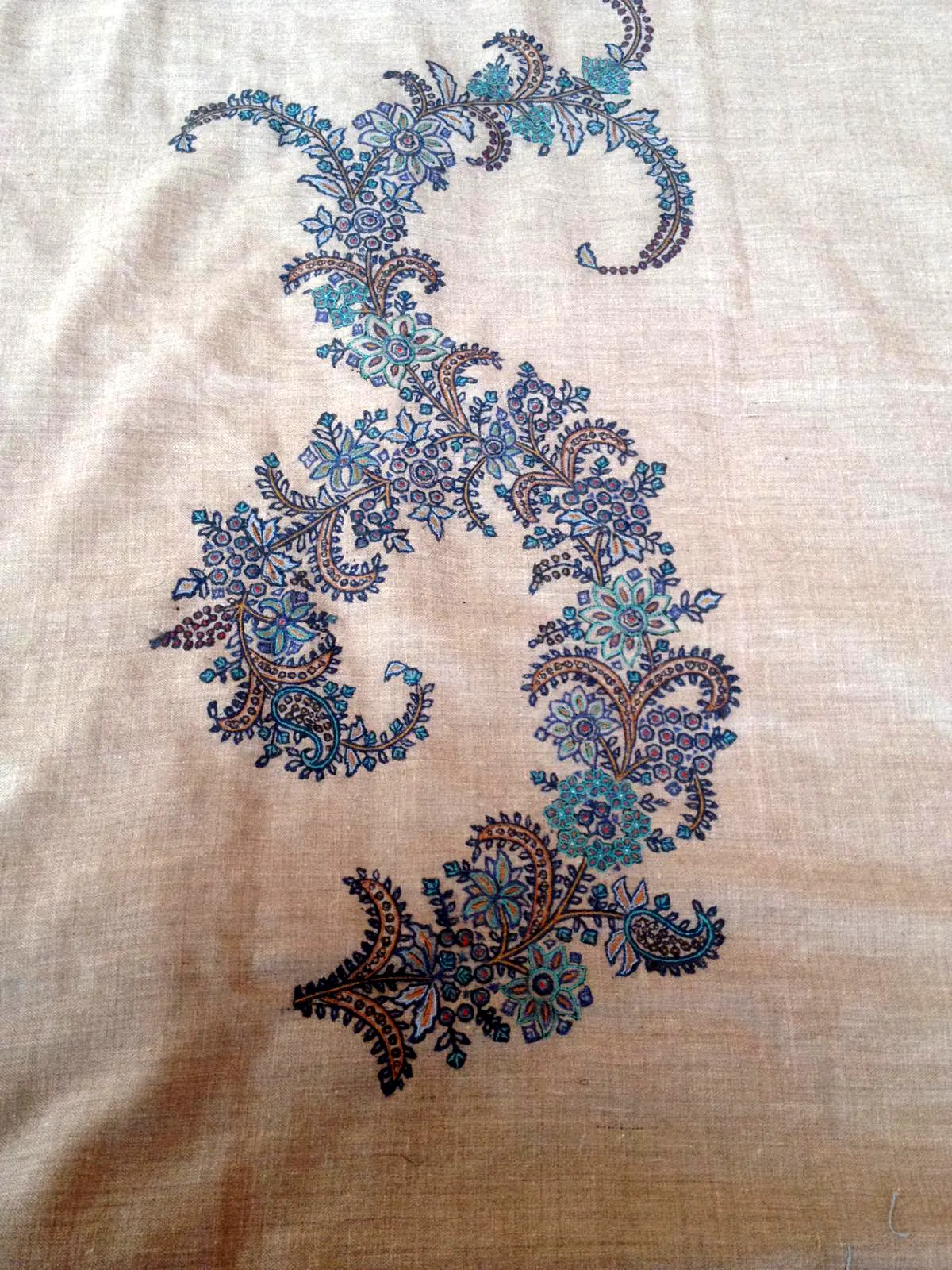 A curling vine of blue and teal needlework on plain beige pashmina.