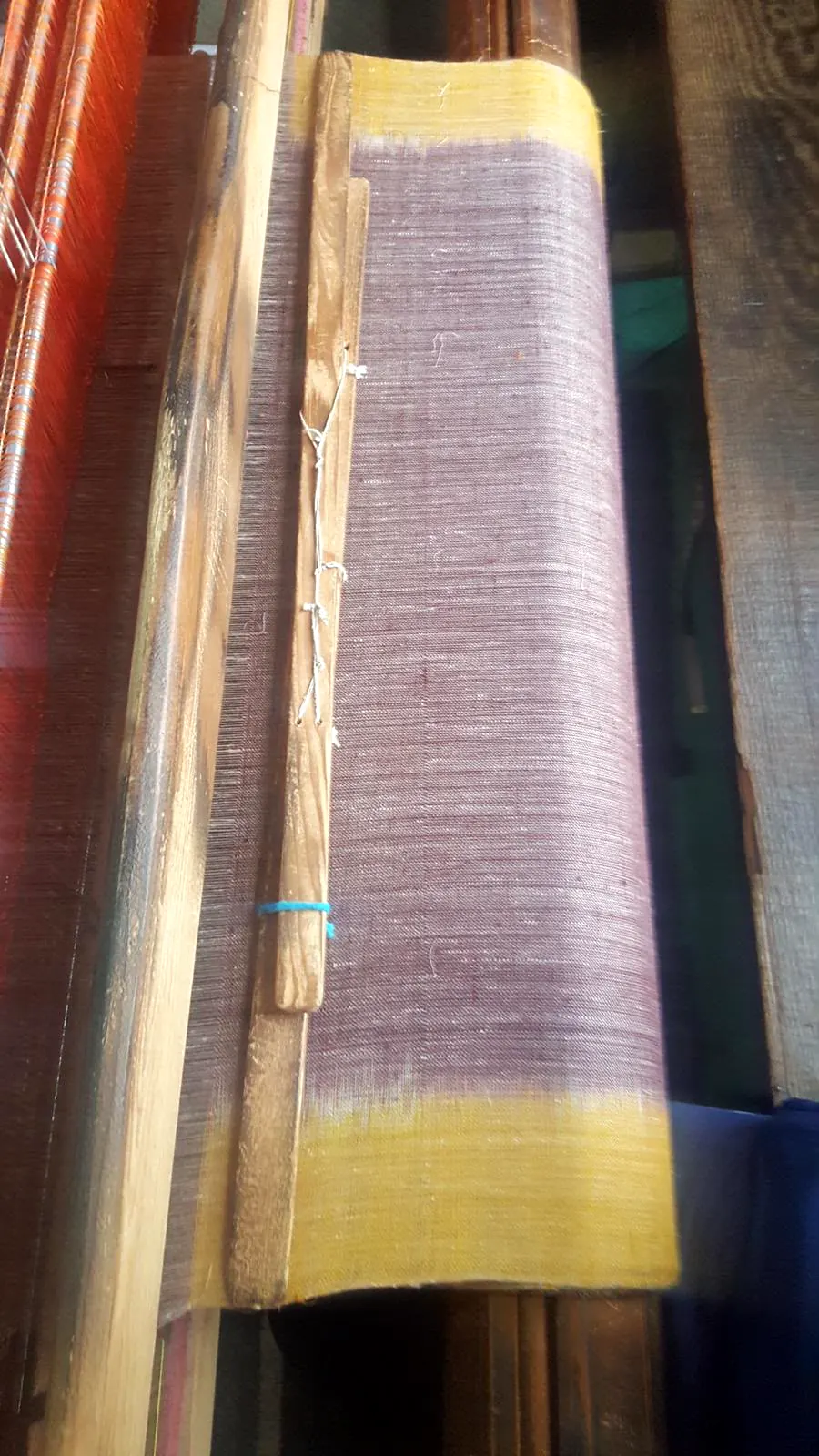 Woven lavender cloth wound on the loom's beam, a yellow band at the edge.
