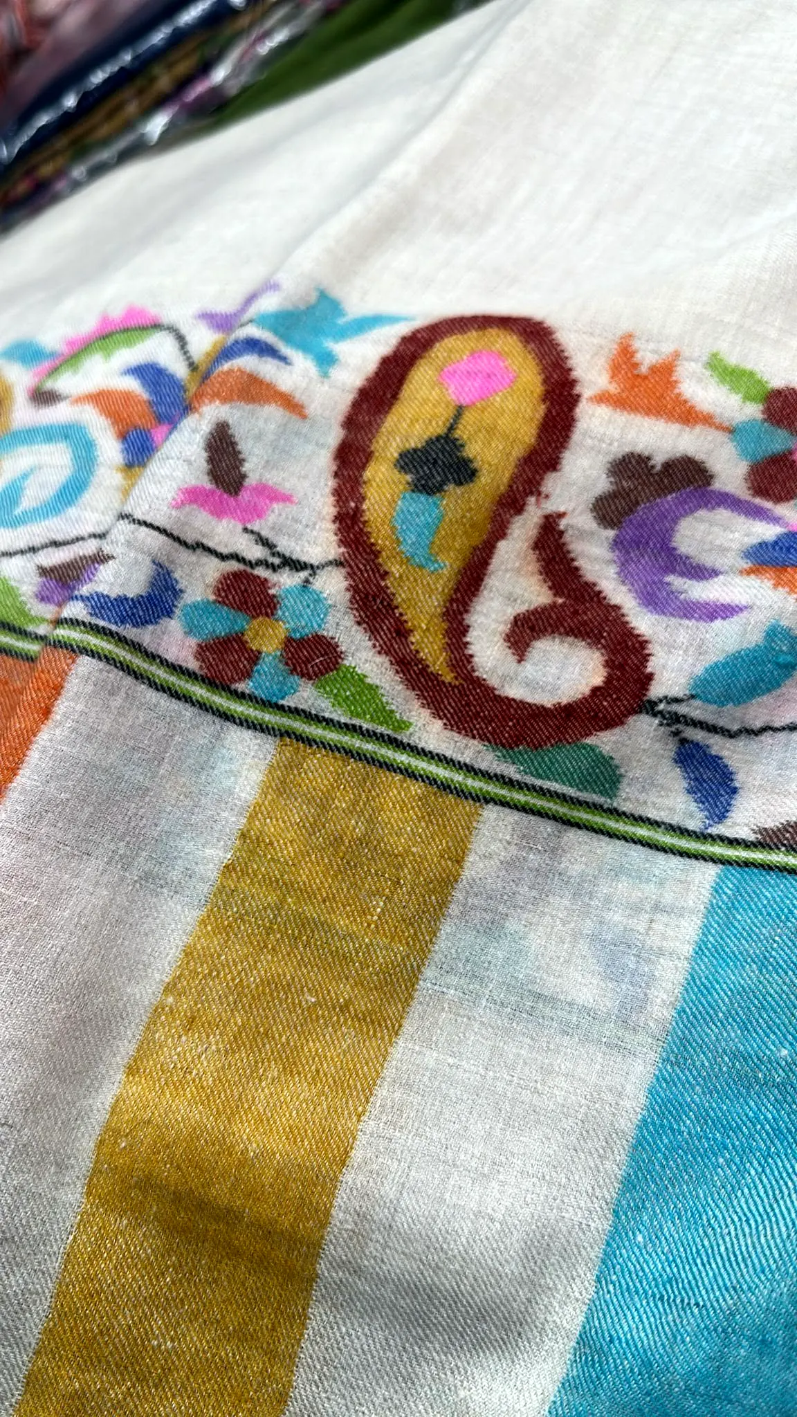 Close view of a kani paisley woven in blue, pink and green above yellow and blue stripes.