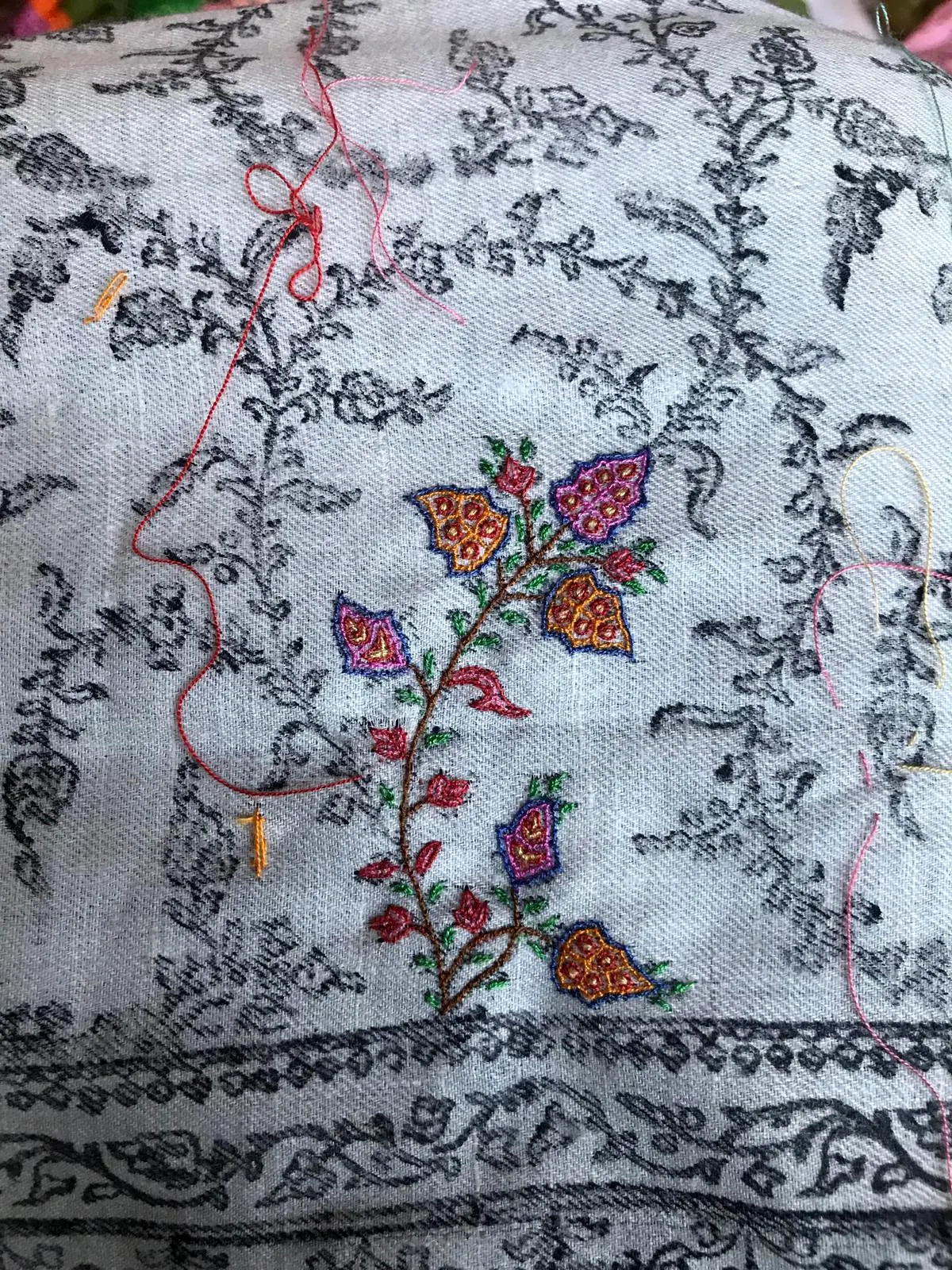 A grey printed pattern on ivory cloth, with a few flowers already embroidered in colour and threads left hanging.