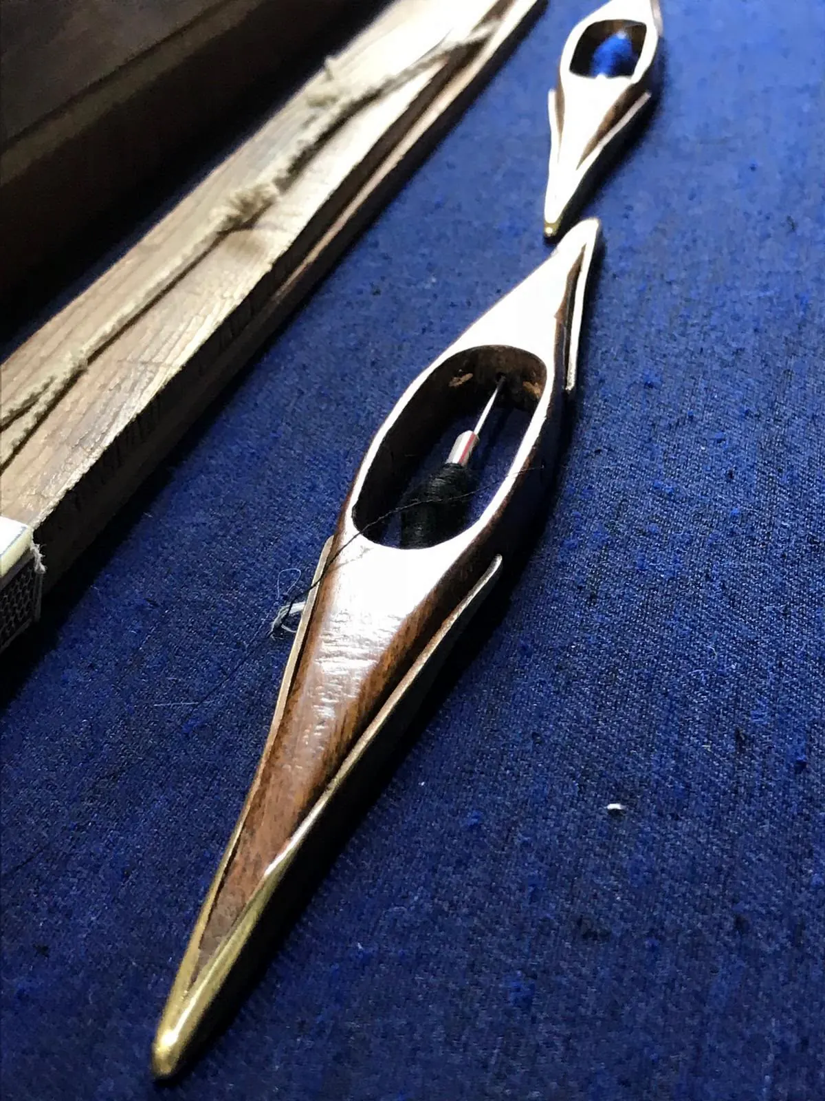 A wooden shuttle resting on dark blue cloth on the loom.