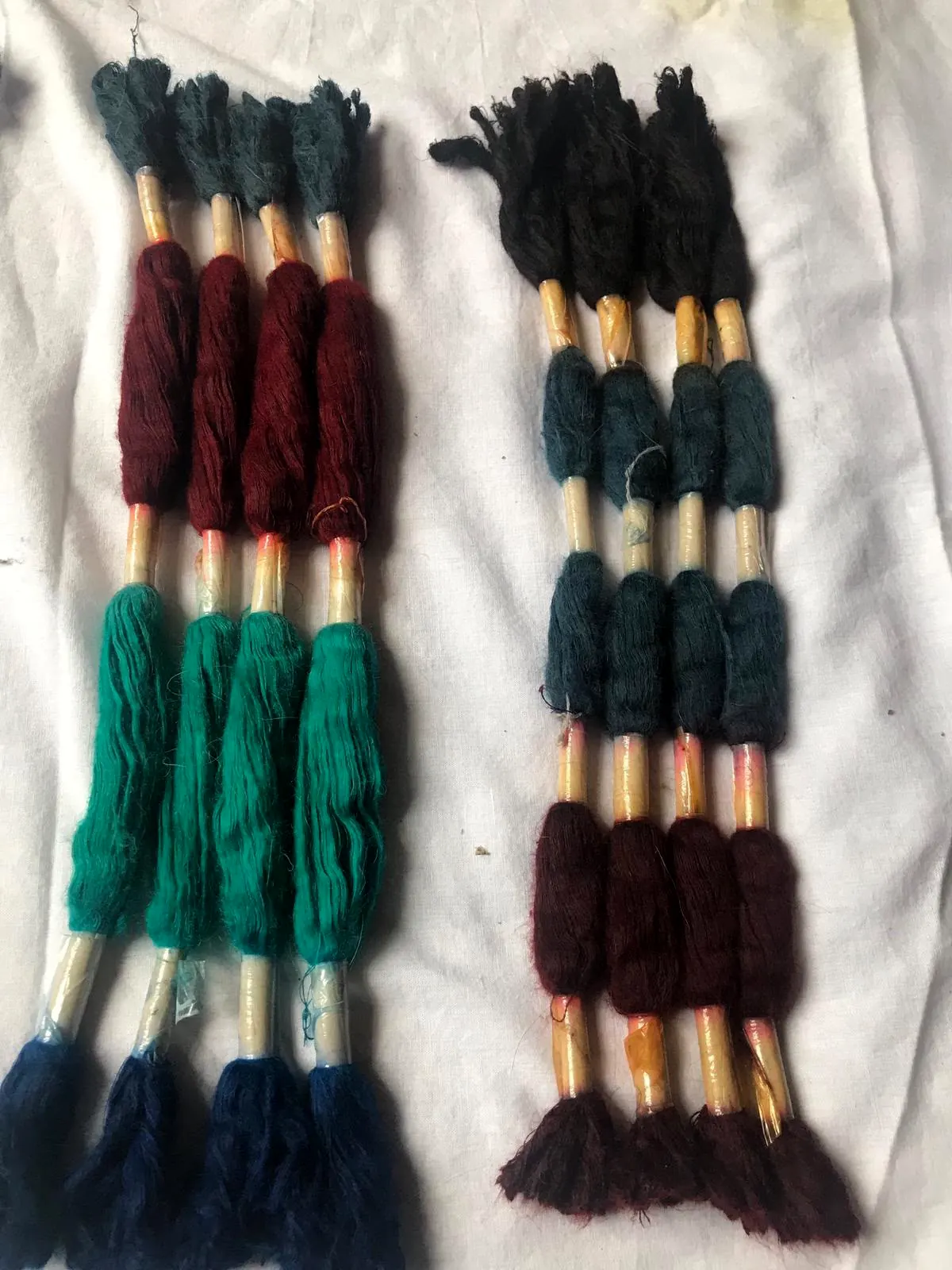 Skeins of teal, green, maroon and navy thread tied in bundles on a white cloth.