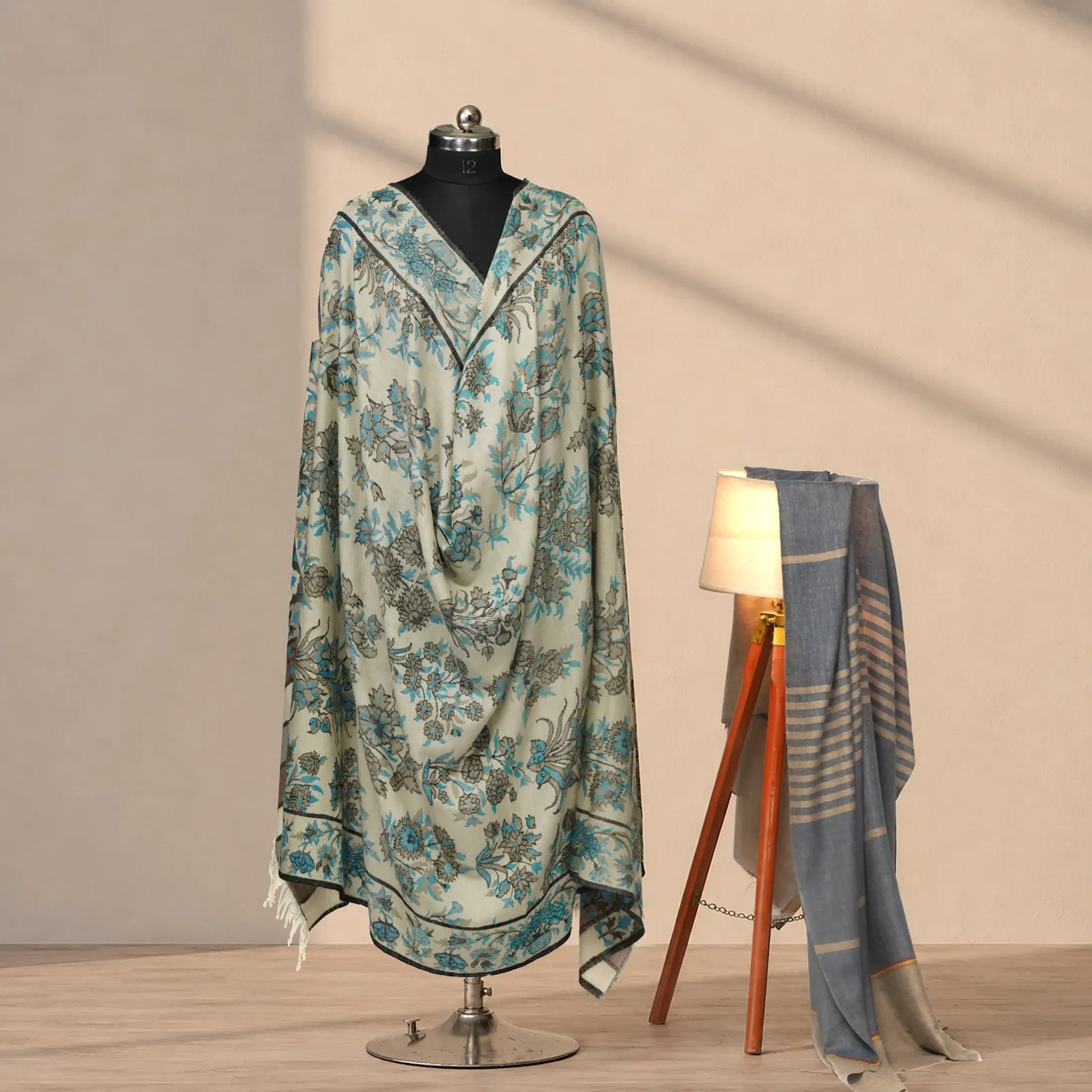 Ivory shawl with an all-over floral in teal and soft brown, a striped grey shawl on a stand behind.
