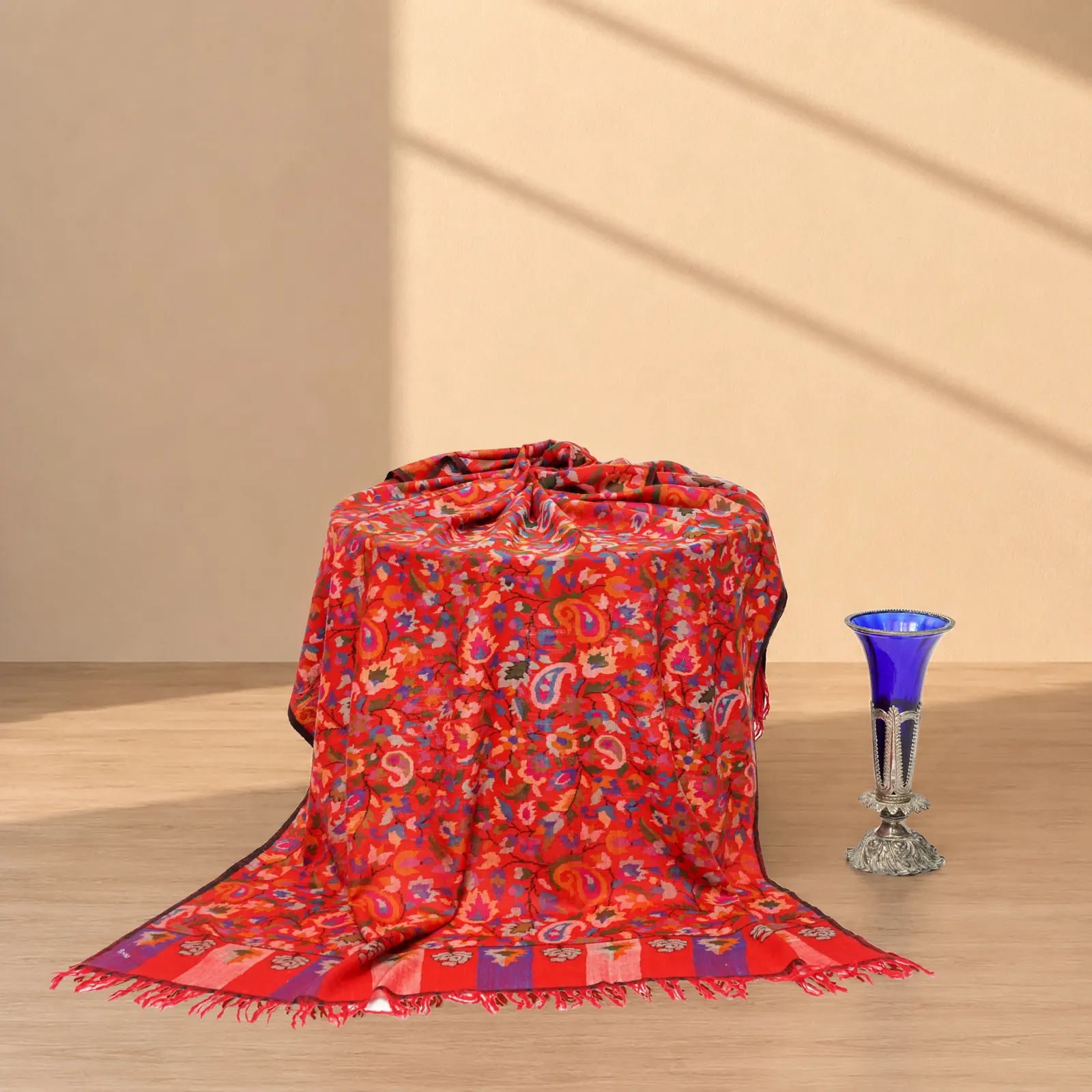 The same scarlet shawl draped over a form beside a blue glass vase.