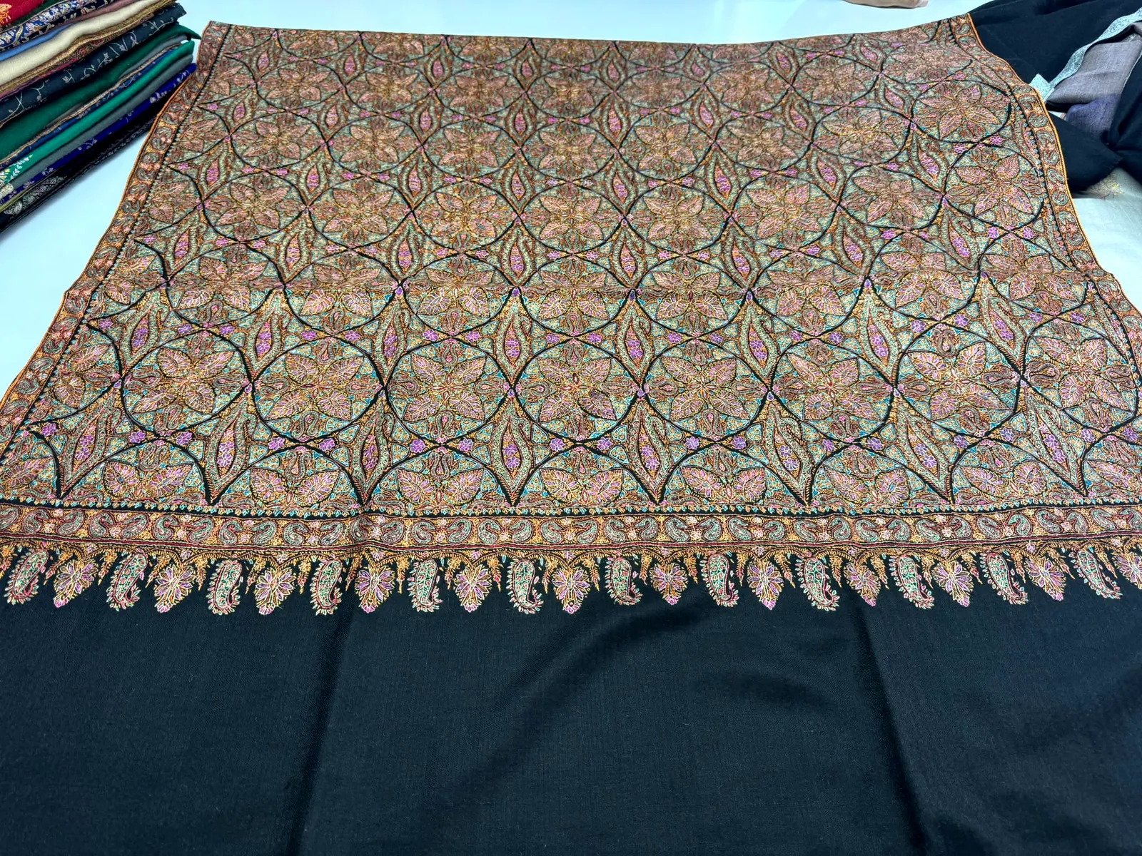 Black shawl with a dense multicoloured lattice of needlework and a paisley border.