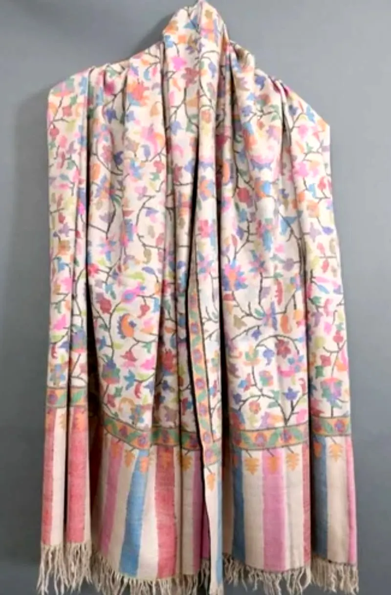 Ivory kani shawl covered in small pink, blue and lilac flowers, hung against a grey wall, with pastel striped ends.