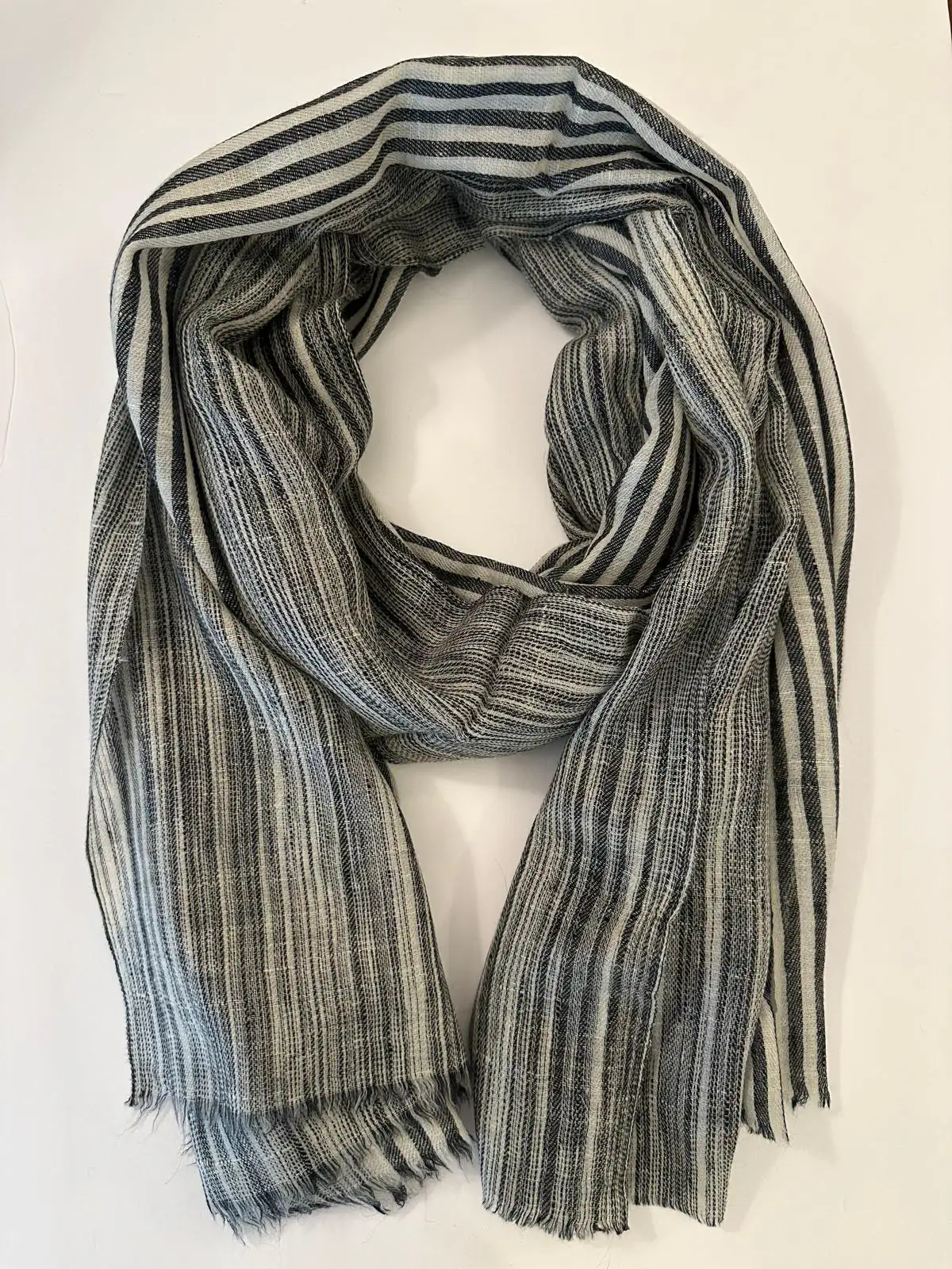 Stole in fine charcoal, grey and ivory stripes, loosely coiled on a white surface.