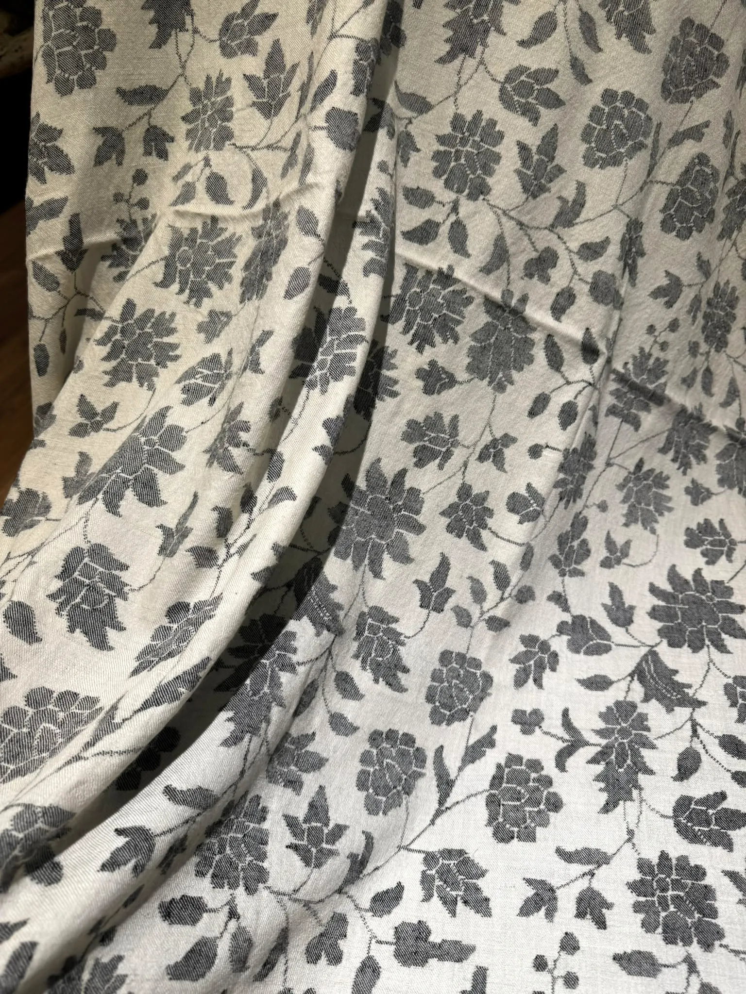 Close view of an ivory kani shawl covered in woven charcoal flowers.