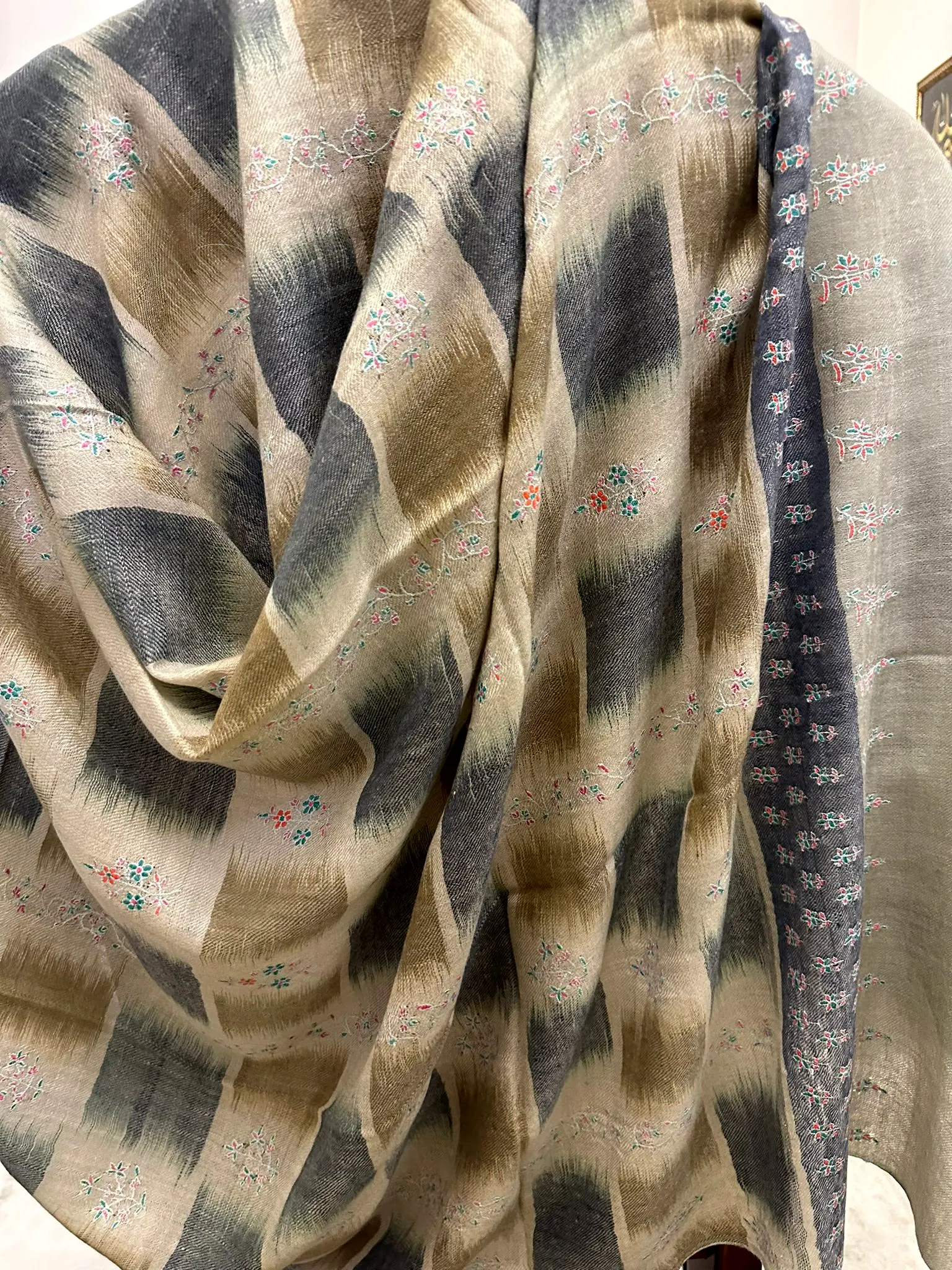 Shawl in grey and beige ikat blocks with small coloured needlework, draped.