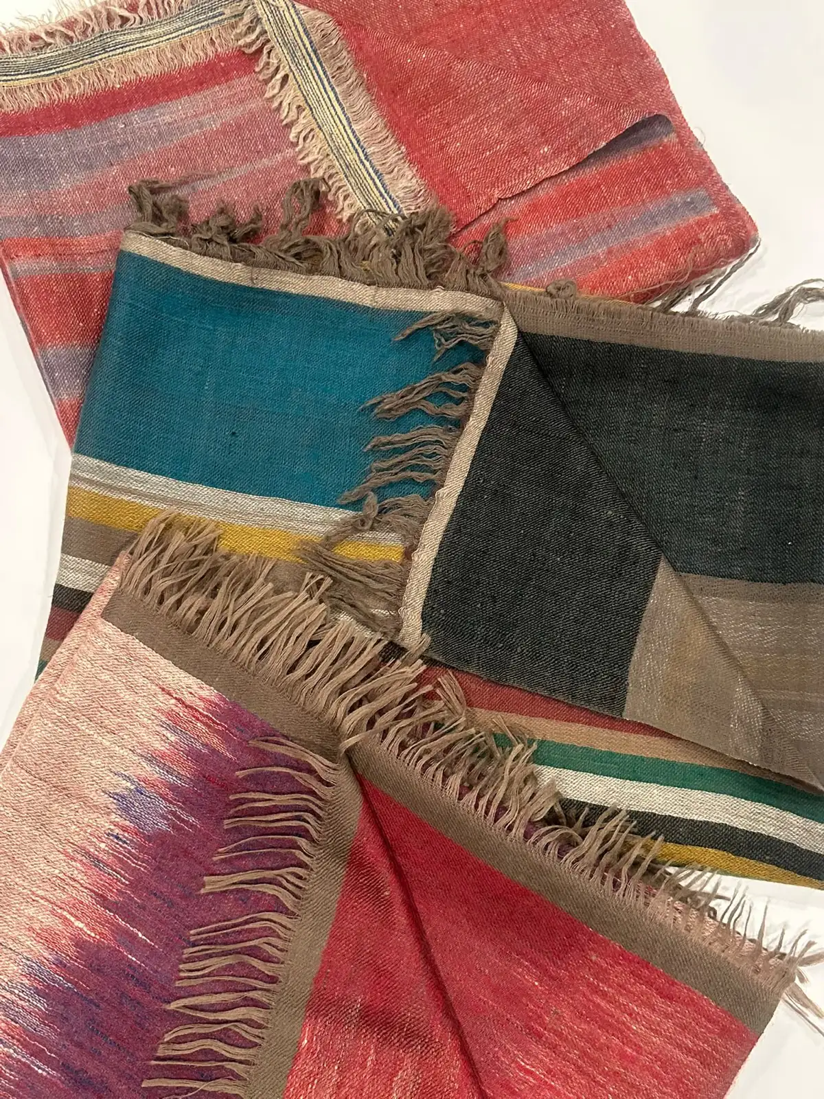 Ikat and striped stoles in red, teal and slate, fringed ends showing.