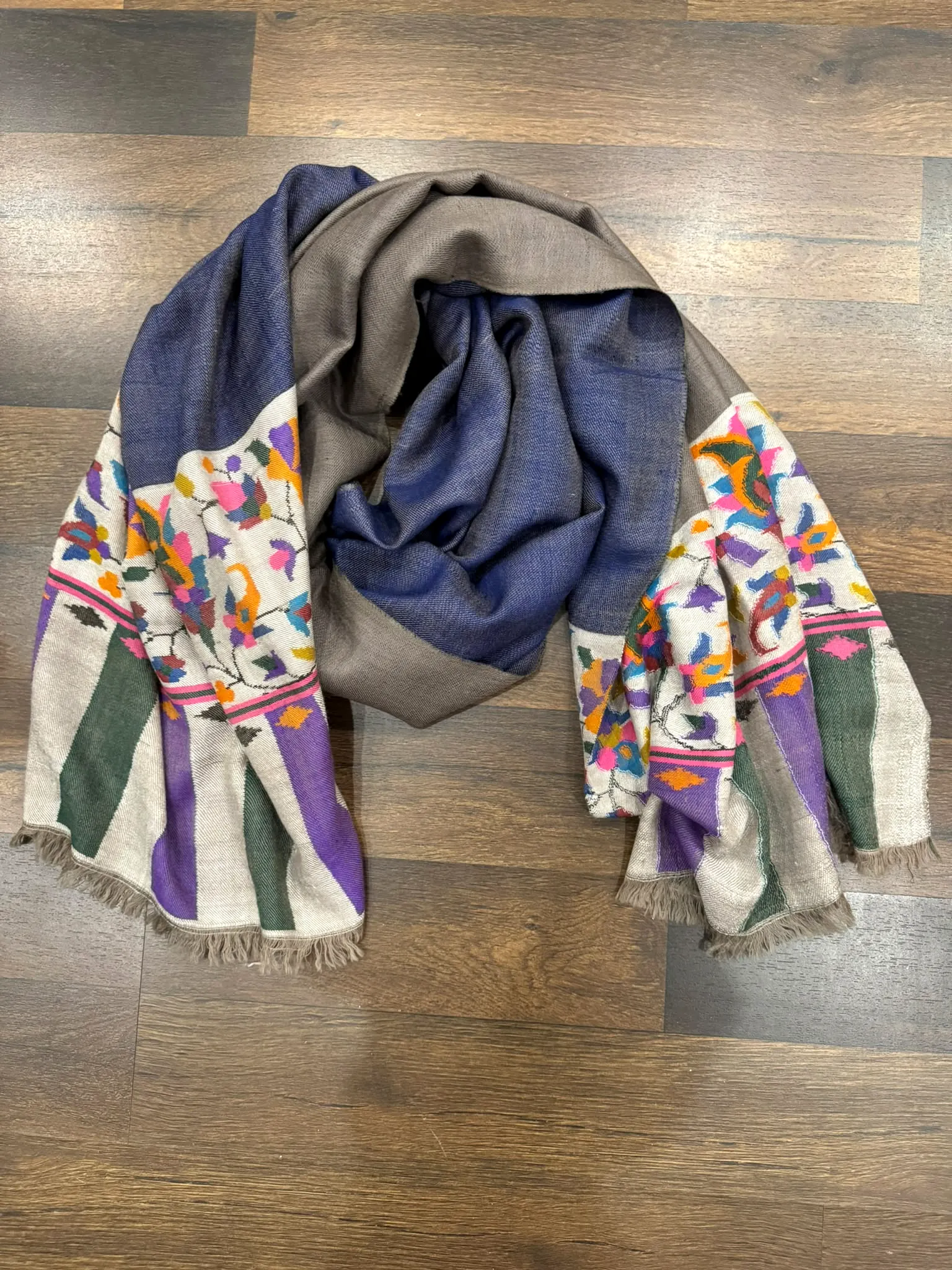 Kani stole with indigo and grey halves and floral and striped ends, on a wooden floor.