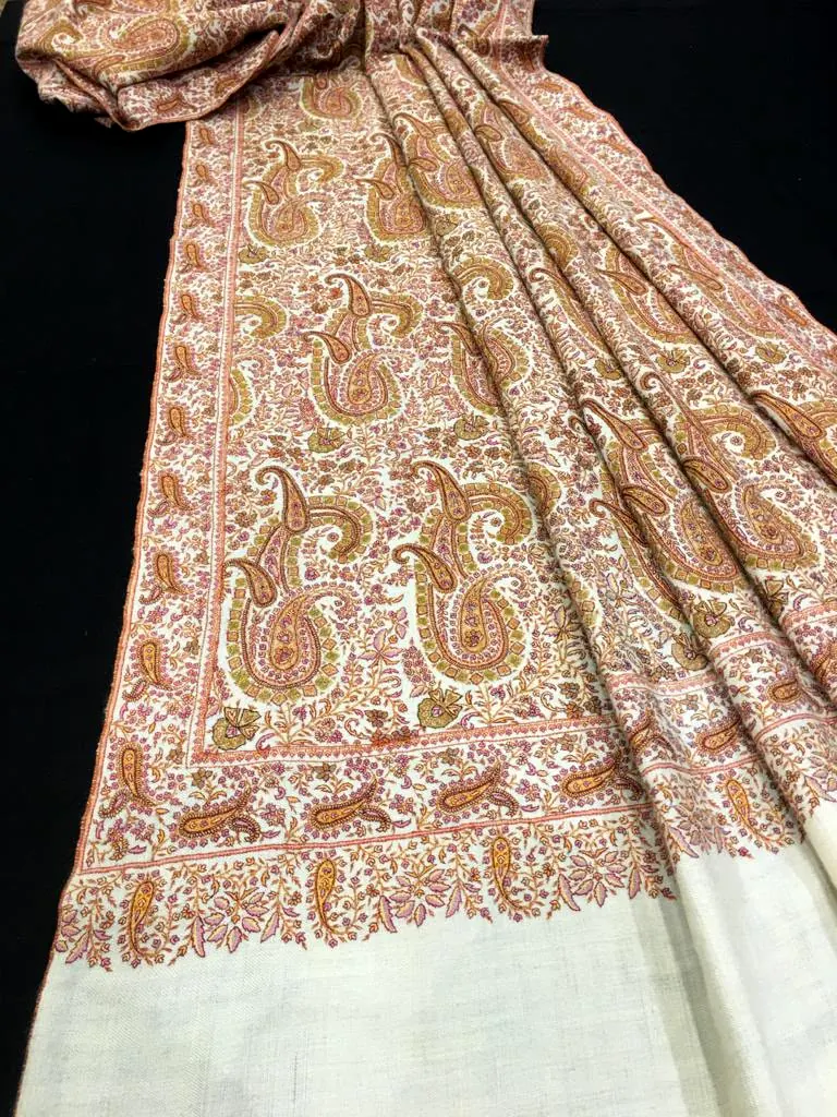 Ivory shawl covered in dense coral and rose paisleys with a plain end, laid on black.