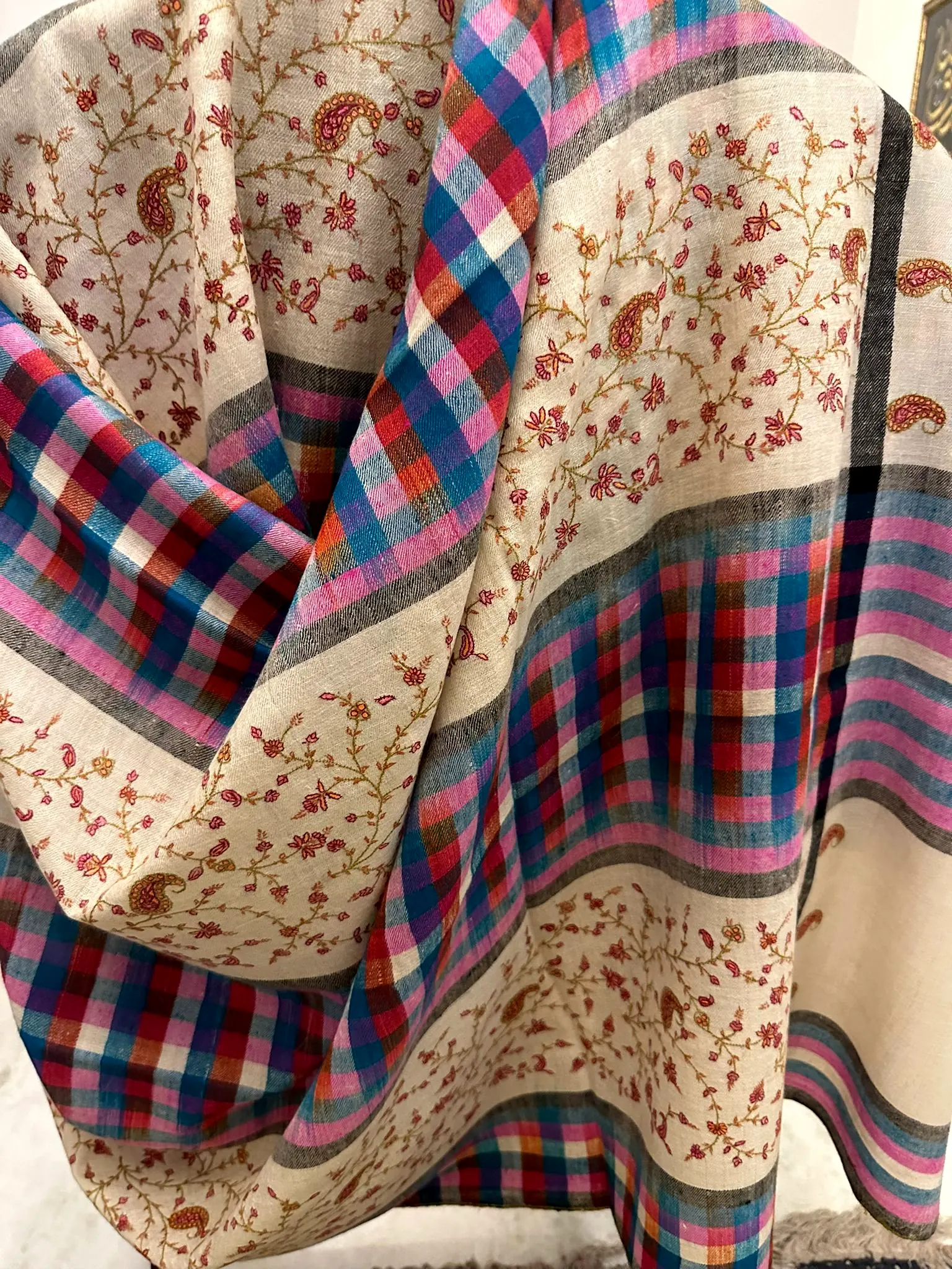 Ivory shawl with pink vine needlework and multicoloured plaid bands, draped.