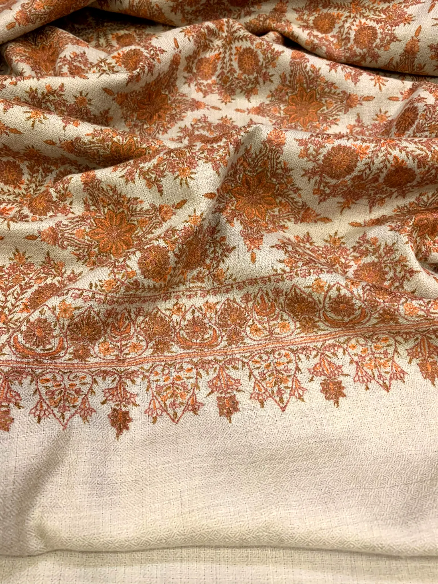 Ivory shawl with a dense field of rust needlework and a scalloped border.