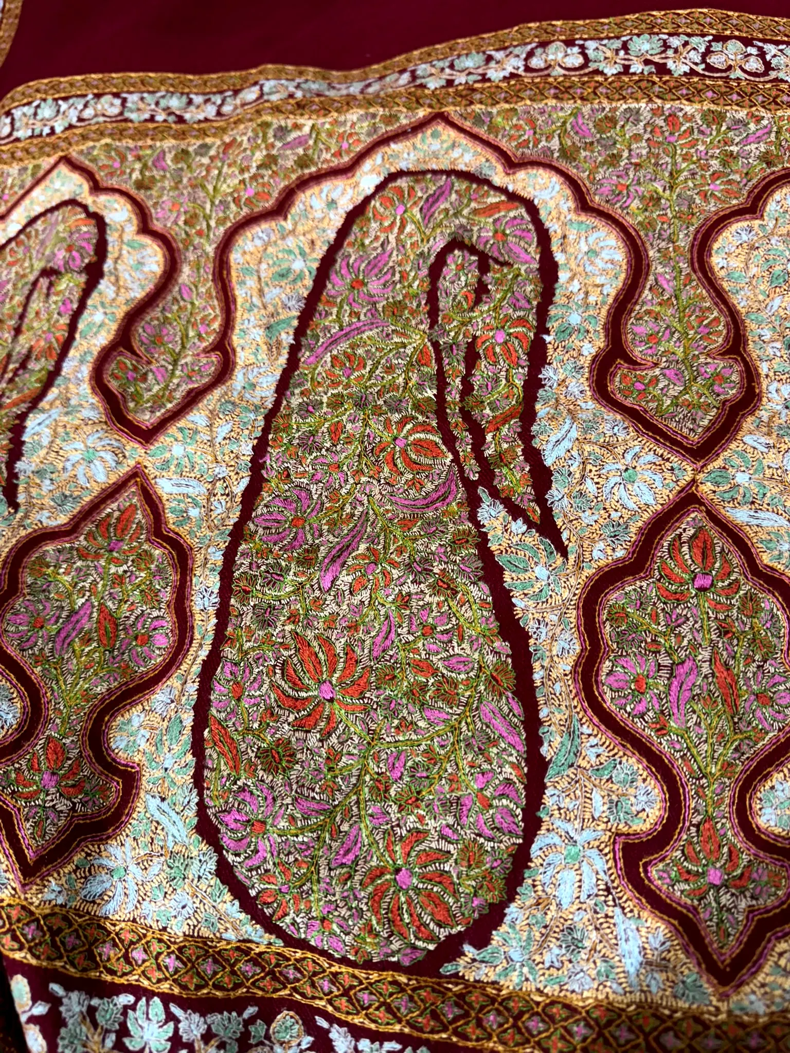 Close view of a maroon shawl with a large paisley filled with fine multicoloured needlework.