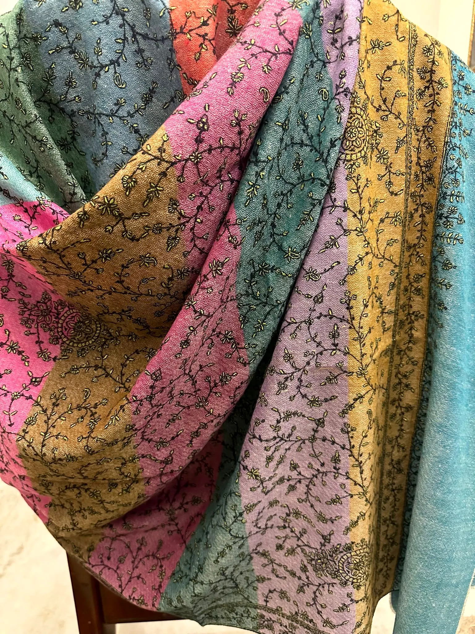 Shawl in pink, grey, mustard and aqua panels covered in black vine needlework, draped.