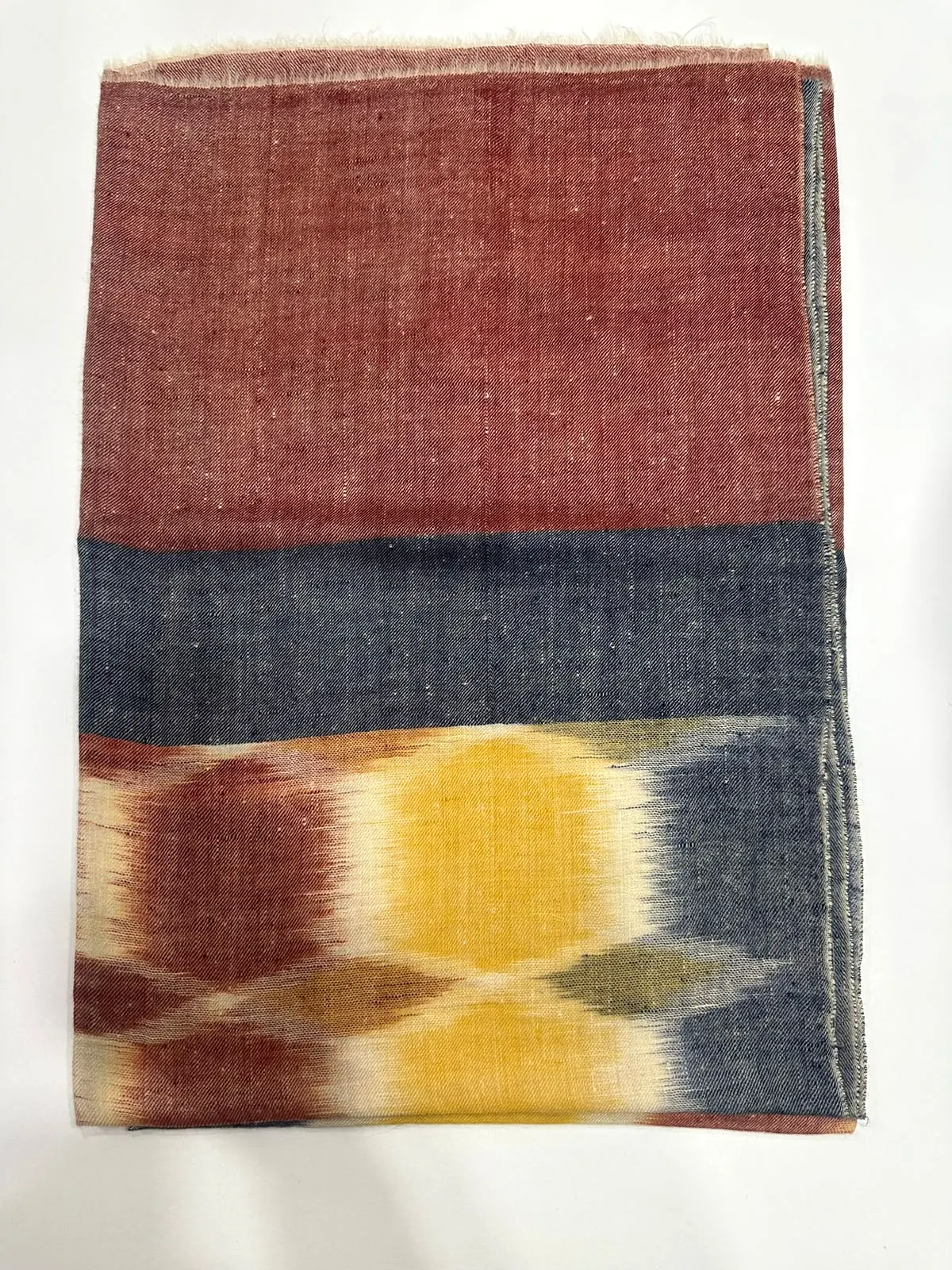 Folded shawl with a rust body, a charcoal band and yellow and maroon ikat motifs.