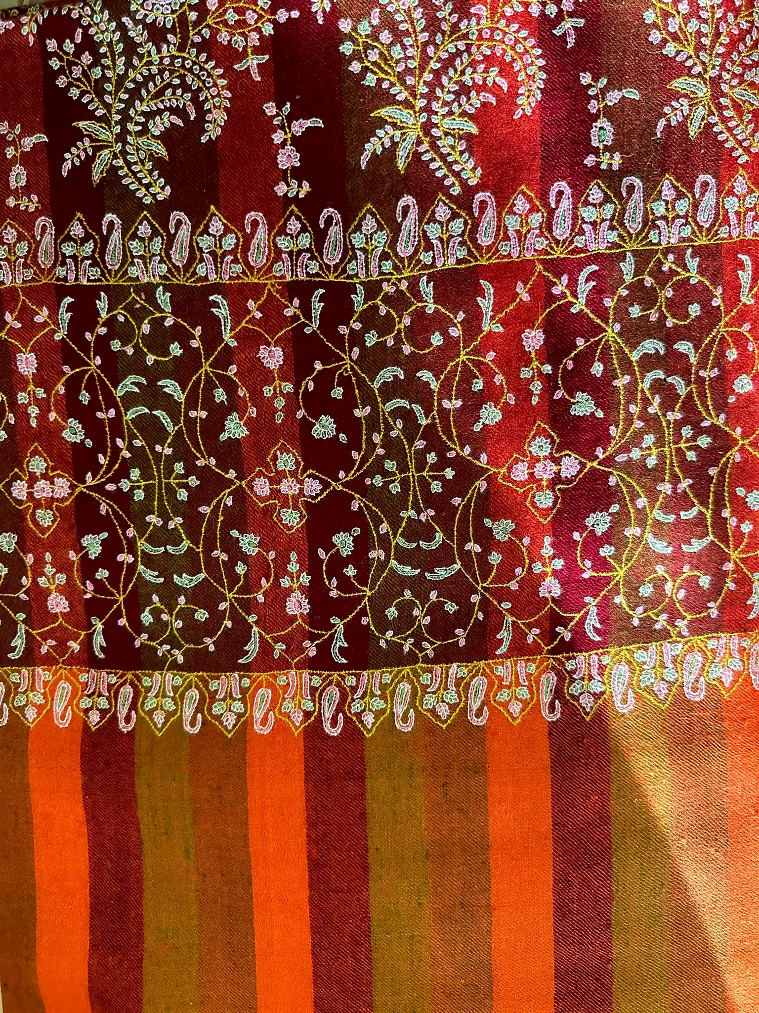 Flat view of the same shawl, showing a maroon field of dense needlework above the orange stripes.