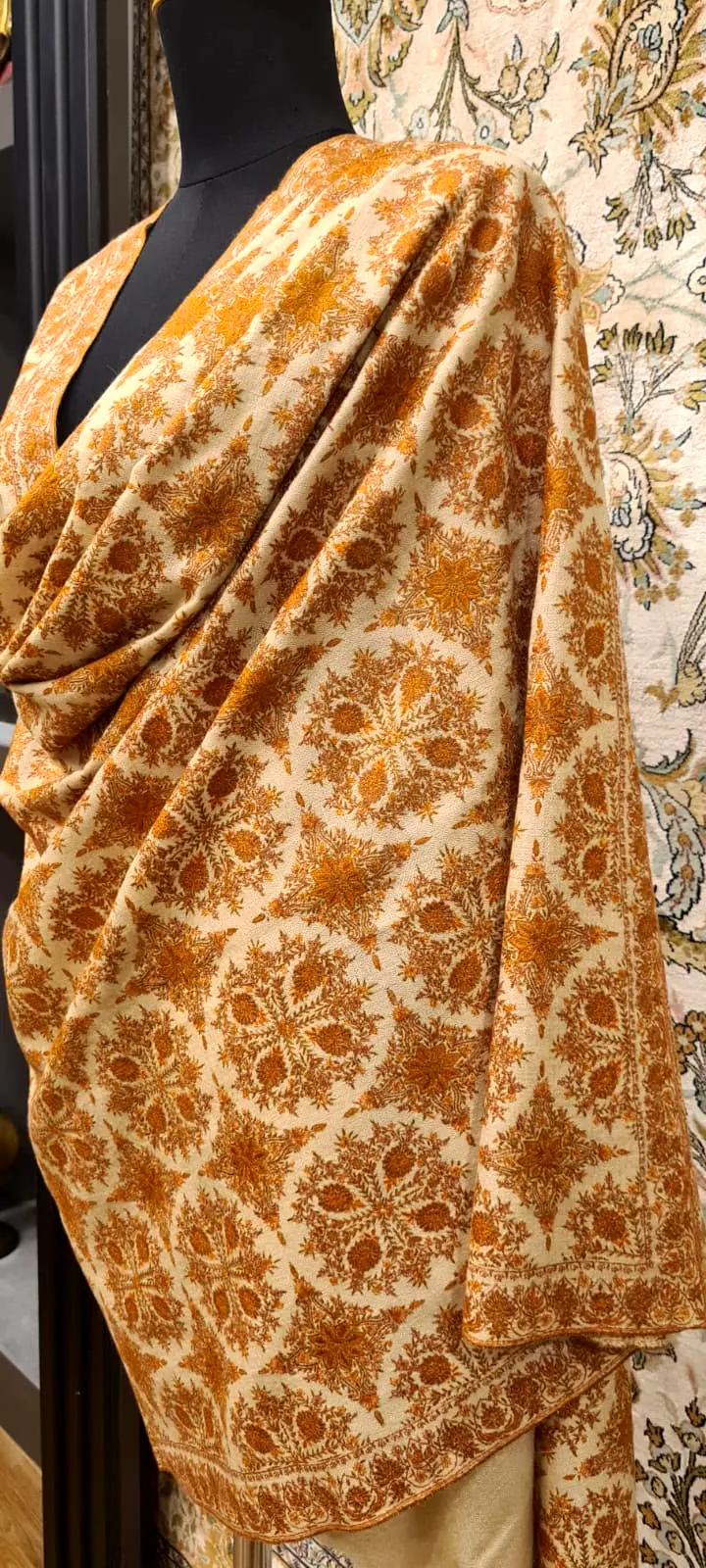 Saffron shawl covered in dense needlework, draped on a stand.