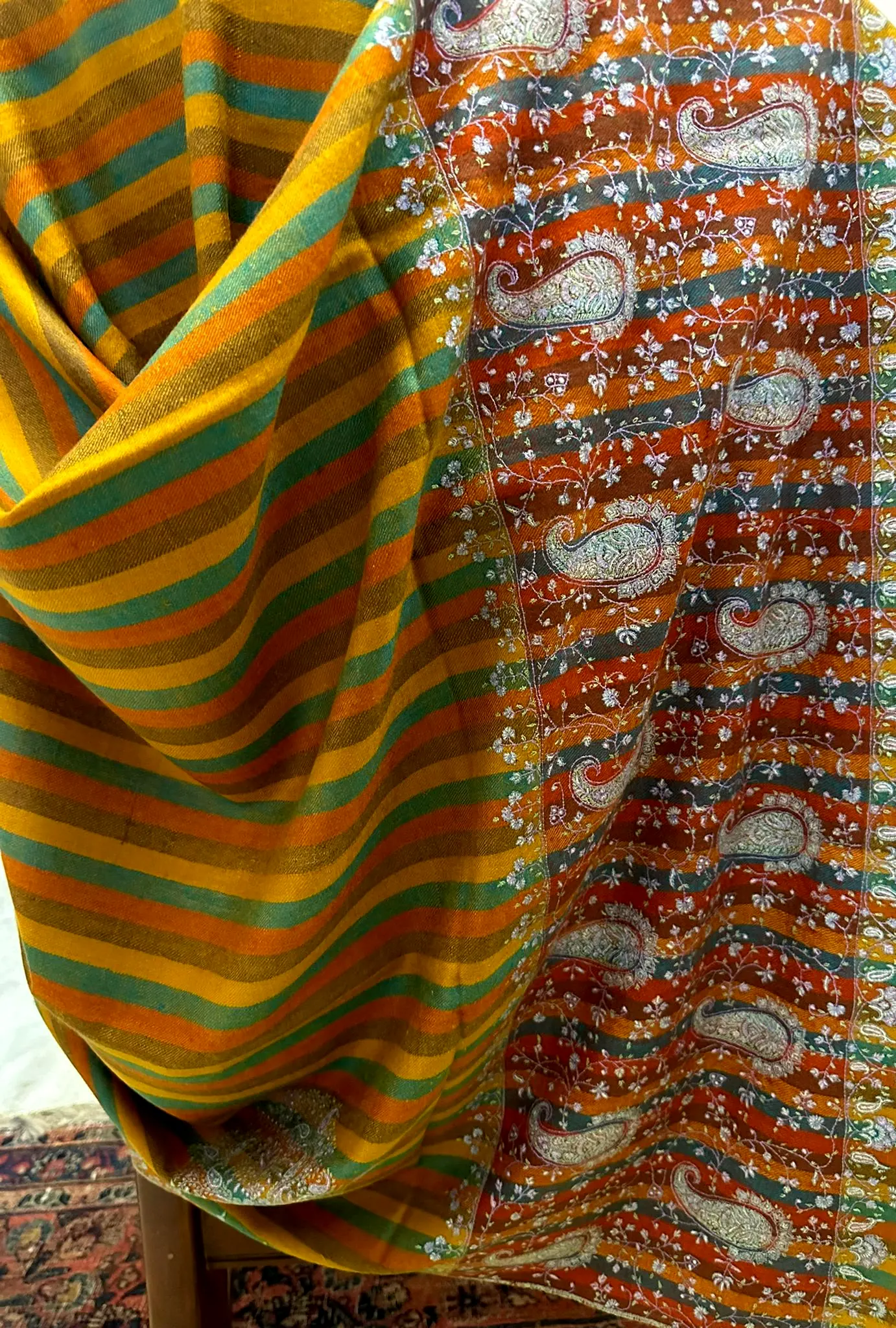 Saffron, orange and teal striped shawl with a band of paisley needlework, draped.