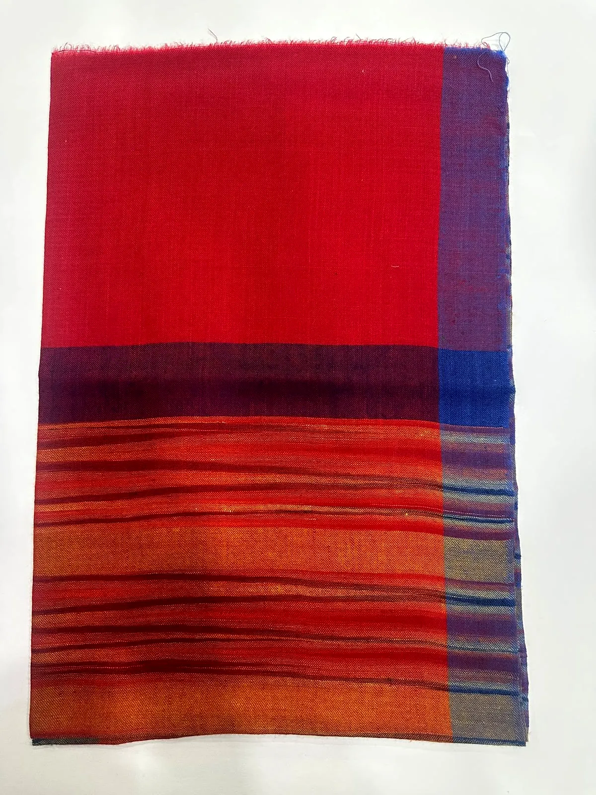 Folded scarlet shawl with a band of orange and red stripes and a blue edge.
