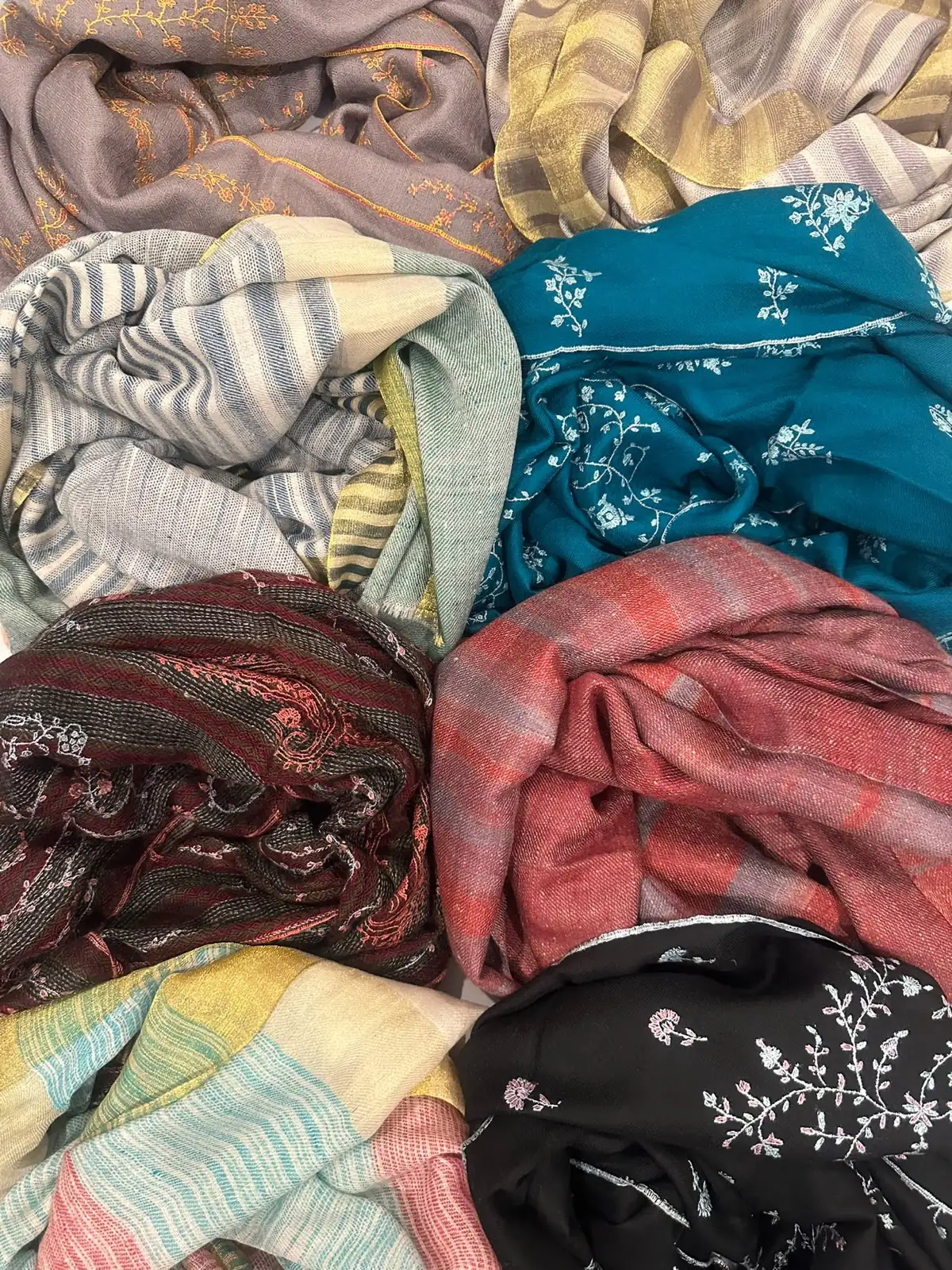 A stack of folded stoles in teal sozni, black sozni, plaid and stripes.