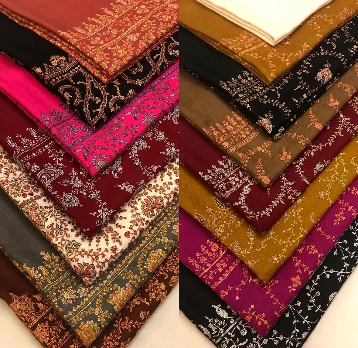 Two stacks of folded shawls in crimson, pink, mustard and black, their corners embroidered.