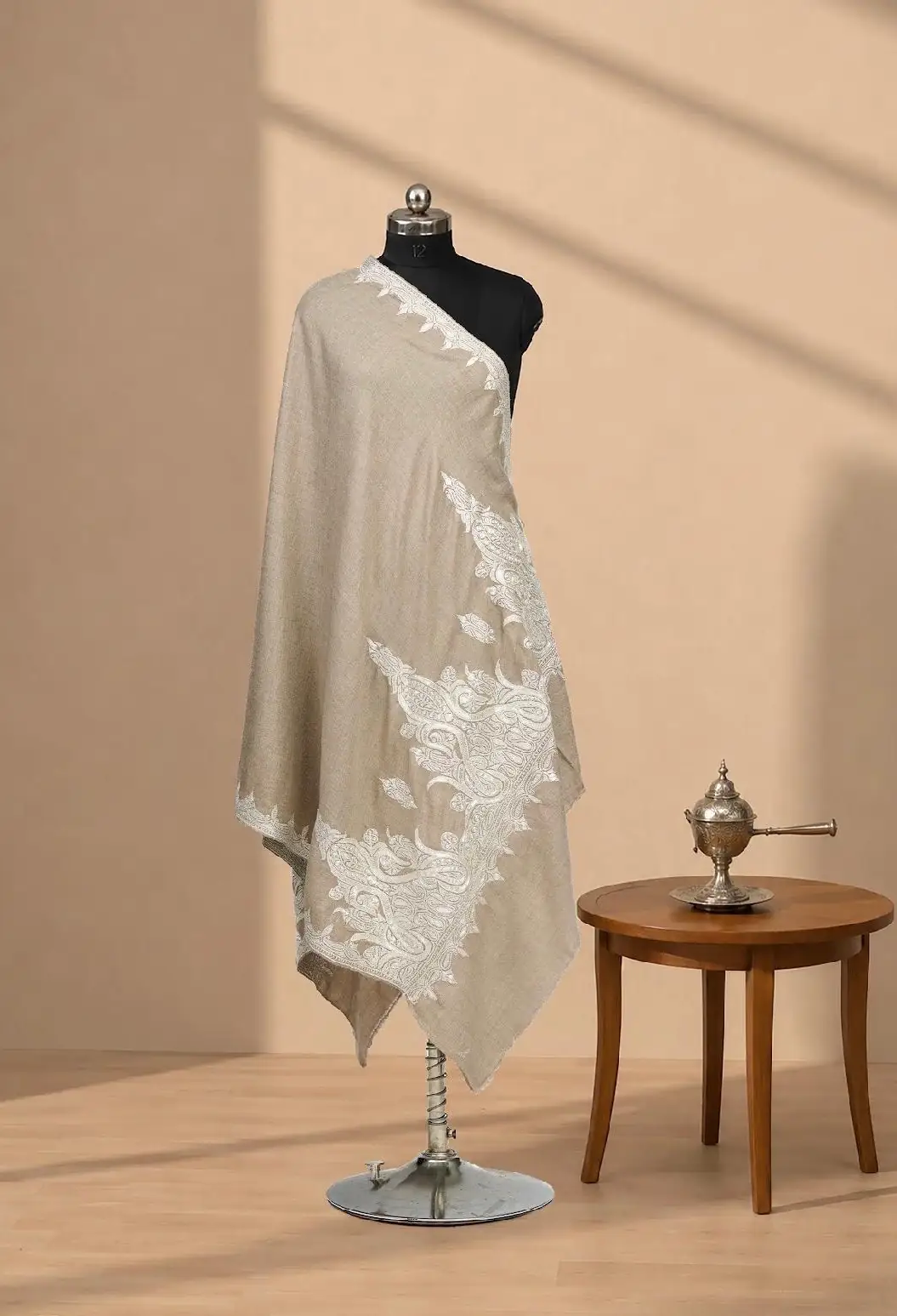 Taupe shawl with a large cream floral motif worked across one corner, on a dress form beside a small silver incense burner.