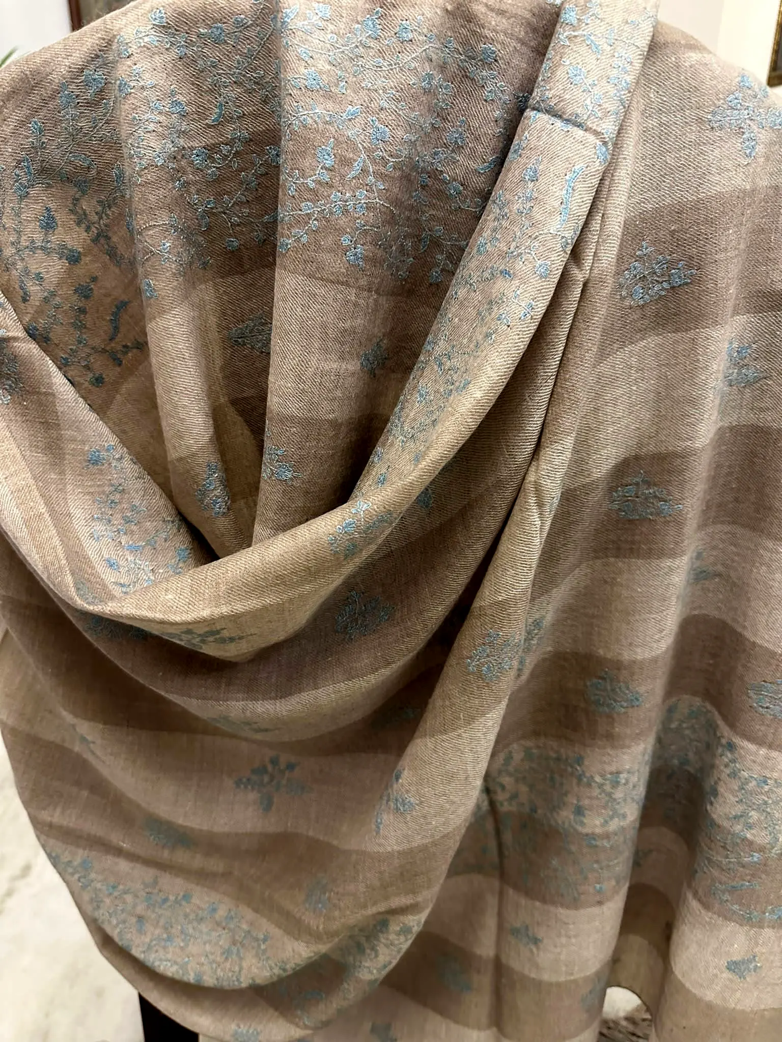 Taupe striped shawl with pale blue needlework motifs, draped.